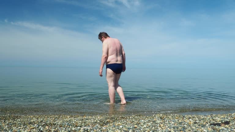 Overweight man is going into the water to swim in the Black sea while exploring Sochi, Russia
